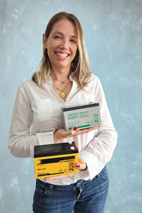 Frau in weißer Bluse hält Batterien in die Kamera